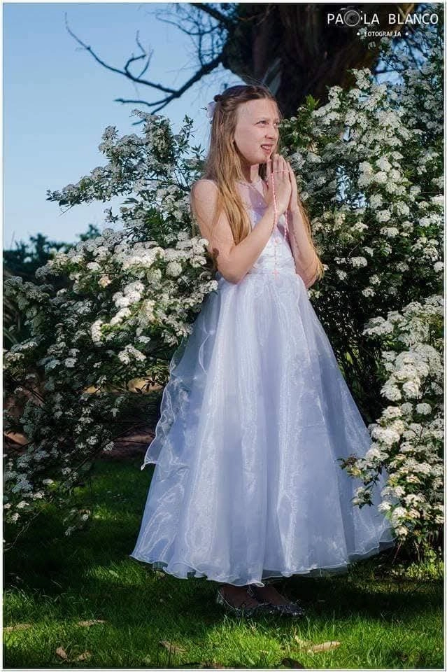 Niña con vestido blanco de comunión entre flores