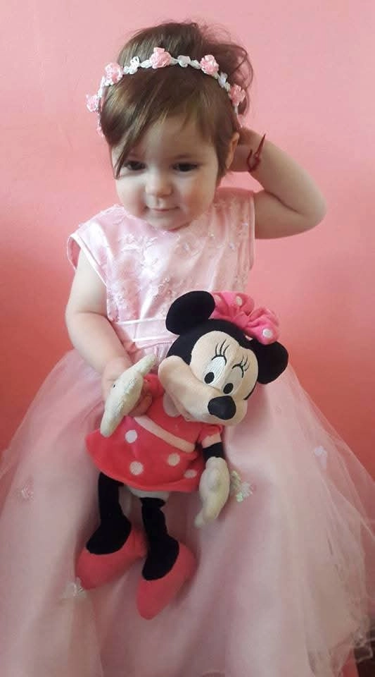 Beba con vestido rosa y muñeco en mano